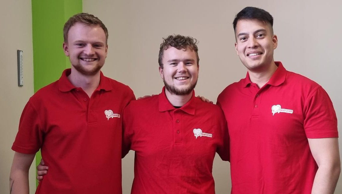 Three men from BCS Business Computer Solutions, wearing red shirts, pose for a photo while volunteering for Community Lifesavers.