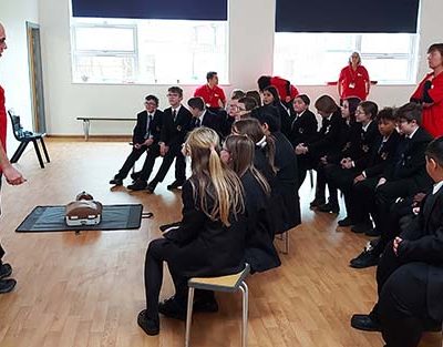 Classroom of students receiving CPR training from Community Lifesavers volunteers.